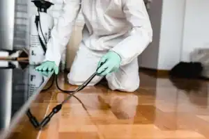 Exterminator from Prestige Pest Unit wearing protective gear, spraying pest control treatment on the floor inside a residential property in Sussex County, New Jersey, to eliminate insects and maintain a safe, pest-free environment.